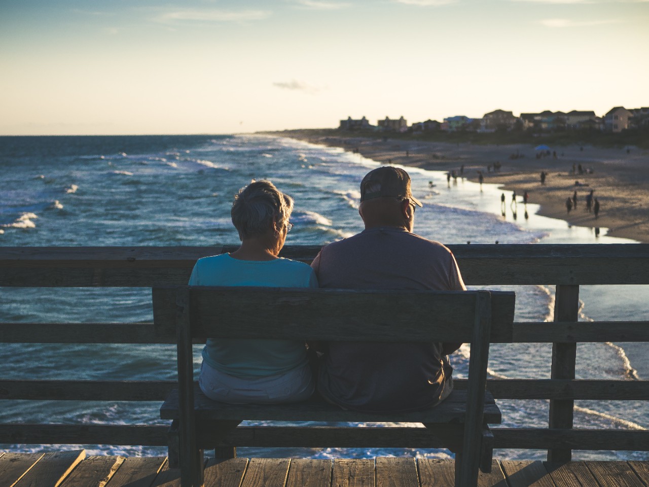 Elderly womand and man, couple, sitting on bench looking out at beach on pier.