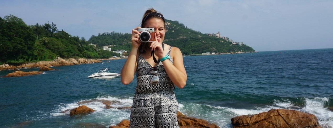 Madison Alvarez aims her camera at the photographer while posing on a rocky beach in Hong Kong. 