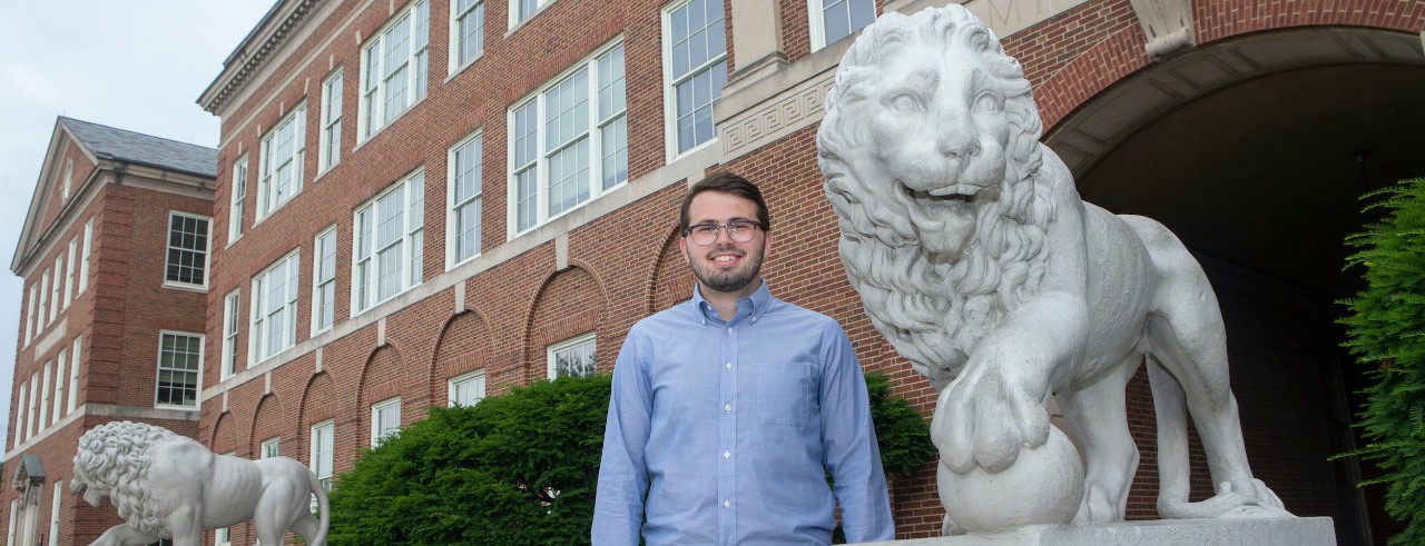 Logan Lindsay poses outside a building between lion statues