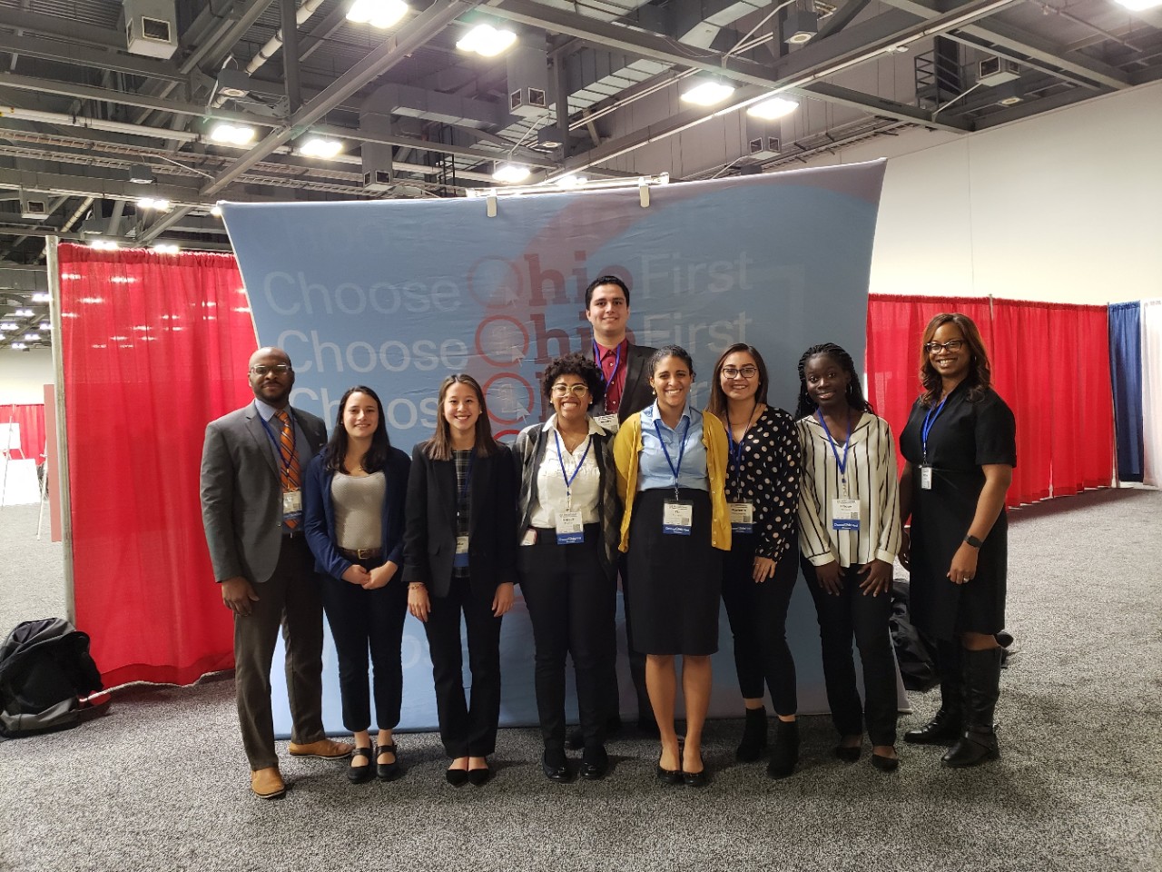 ninepeople standing in an empty convention hall in front of a large display that reads Choose Ohio First