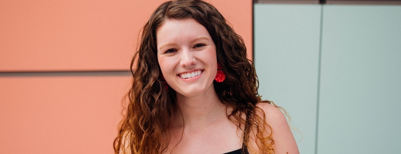 Grace Hertlein stands smiling in front of the DAAP building.