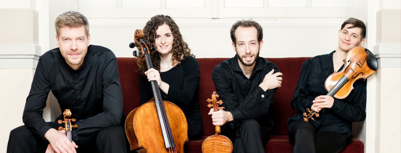 A photograph of the Ariel Quartet, CCM's string quartet-in-residence, sitting on a couch while holding their instruments.
