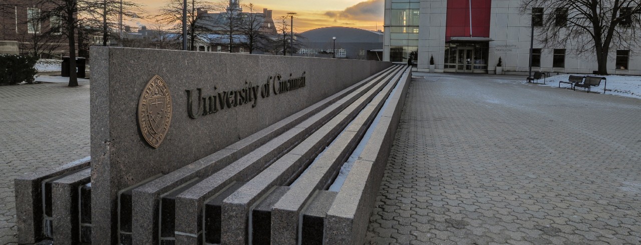 a granite fountain with the letters University of Cincinnati spelled out in front of a large building
