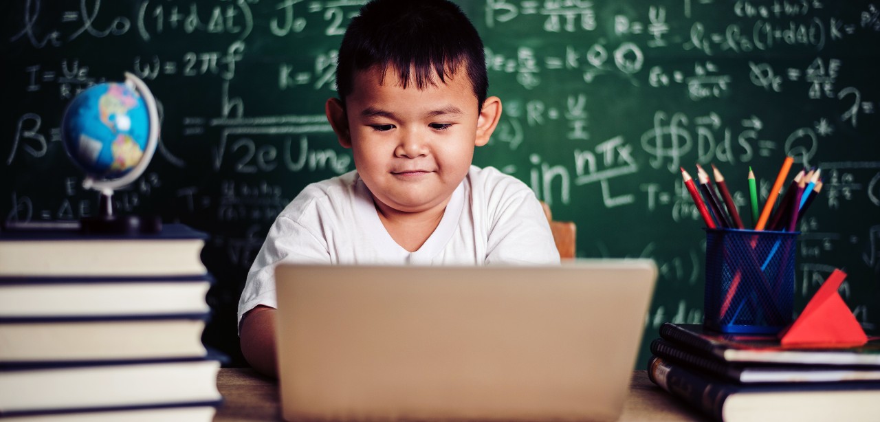 an asian boy uses a laptop in front of a chalkboard