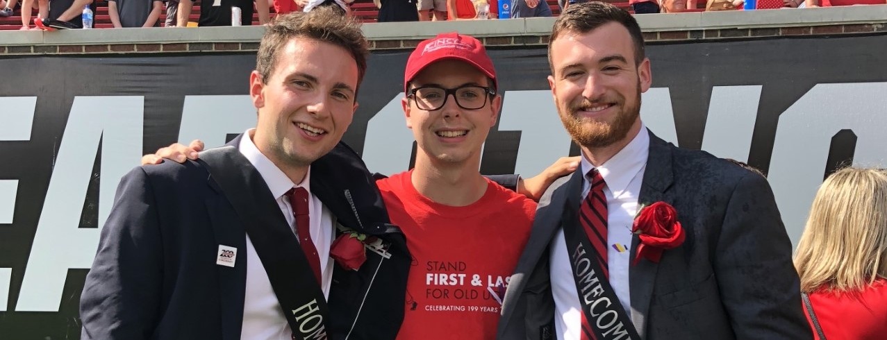 Benjamin Kuhlman stands on the field between two friends on homecoming court.