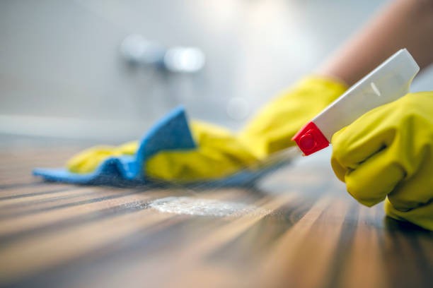 A person spraying disinfectant onto a wooden counter