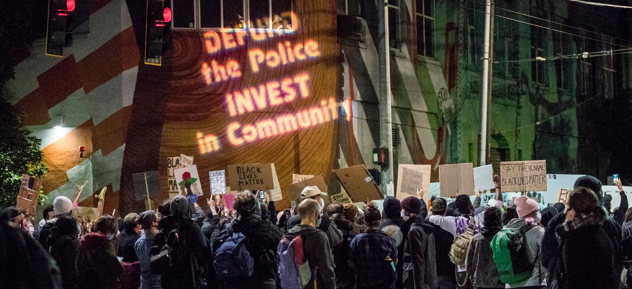 protesters gather on a street at night holding signs in support of Black Lives Matter