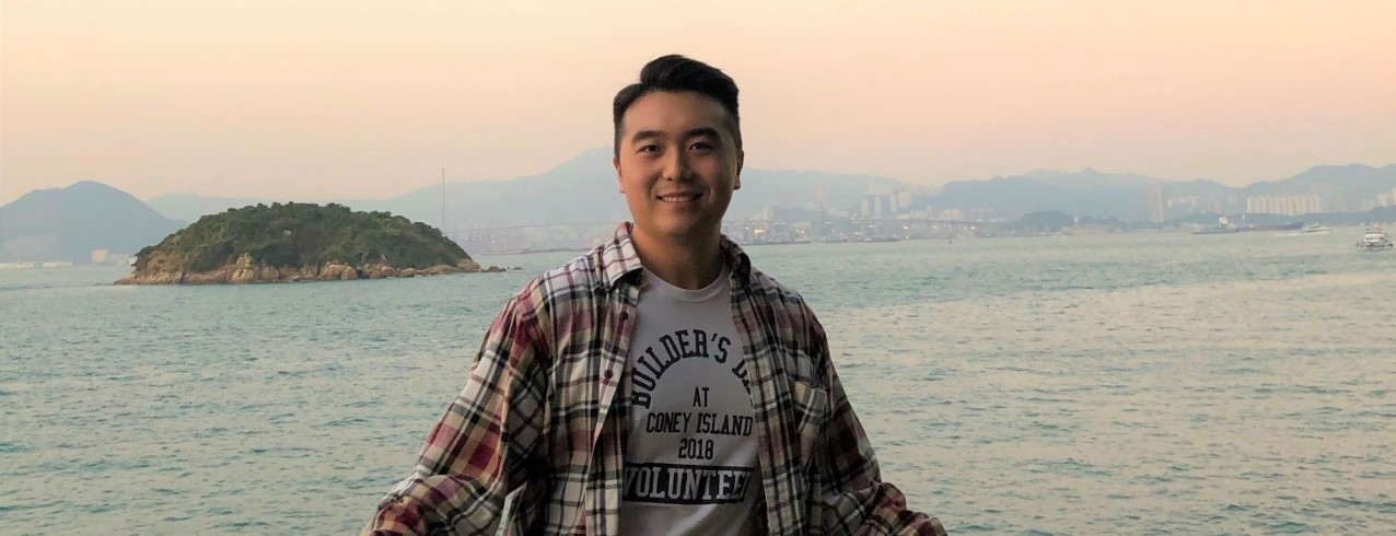 Mark Woo smiles for a photo in Hong Kong in front of a scenic ocean view.