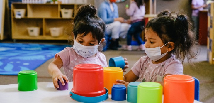 Two children in a pre-school class at Young Horizons play with blocks while wearing facemasks. 
