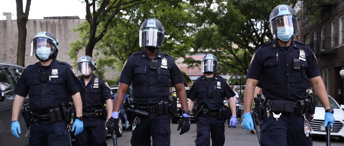 Police officers wearing masks and rubber gloves walk on a city street