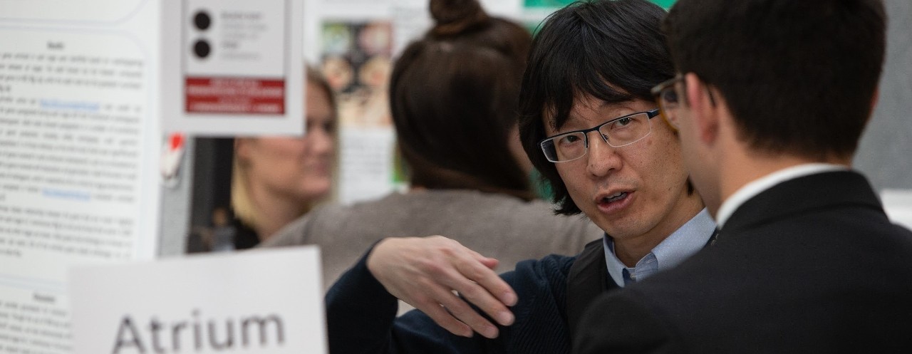 Man with glasses looks inquiringly at a younger man at a research poster showcase