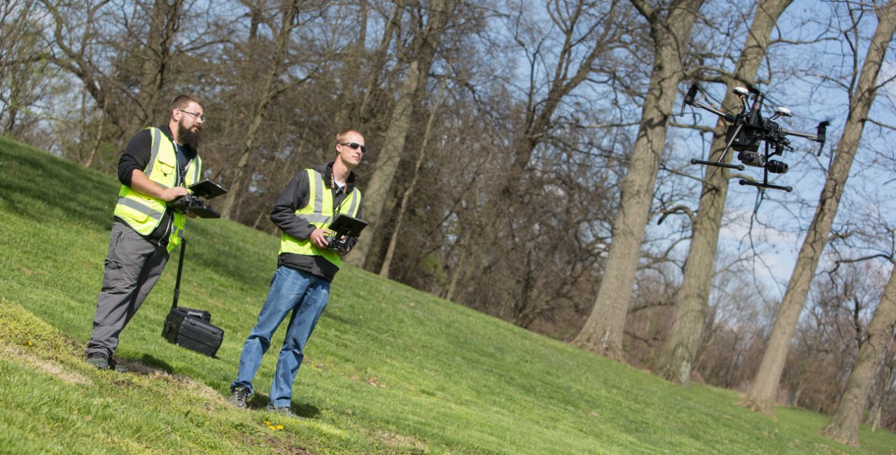 Two people wearing safety vests fly a drone.