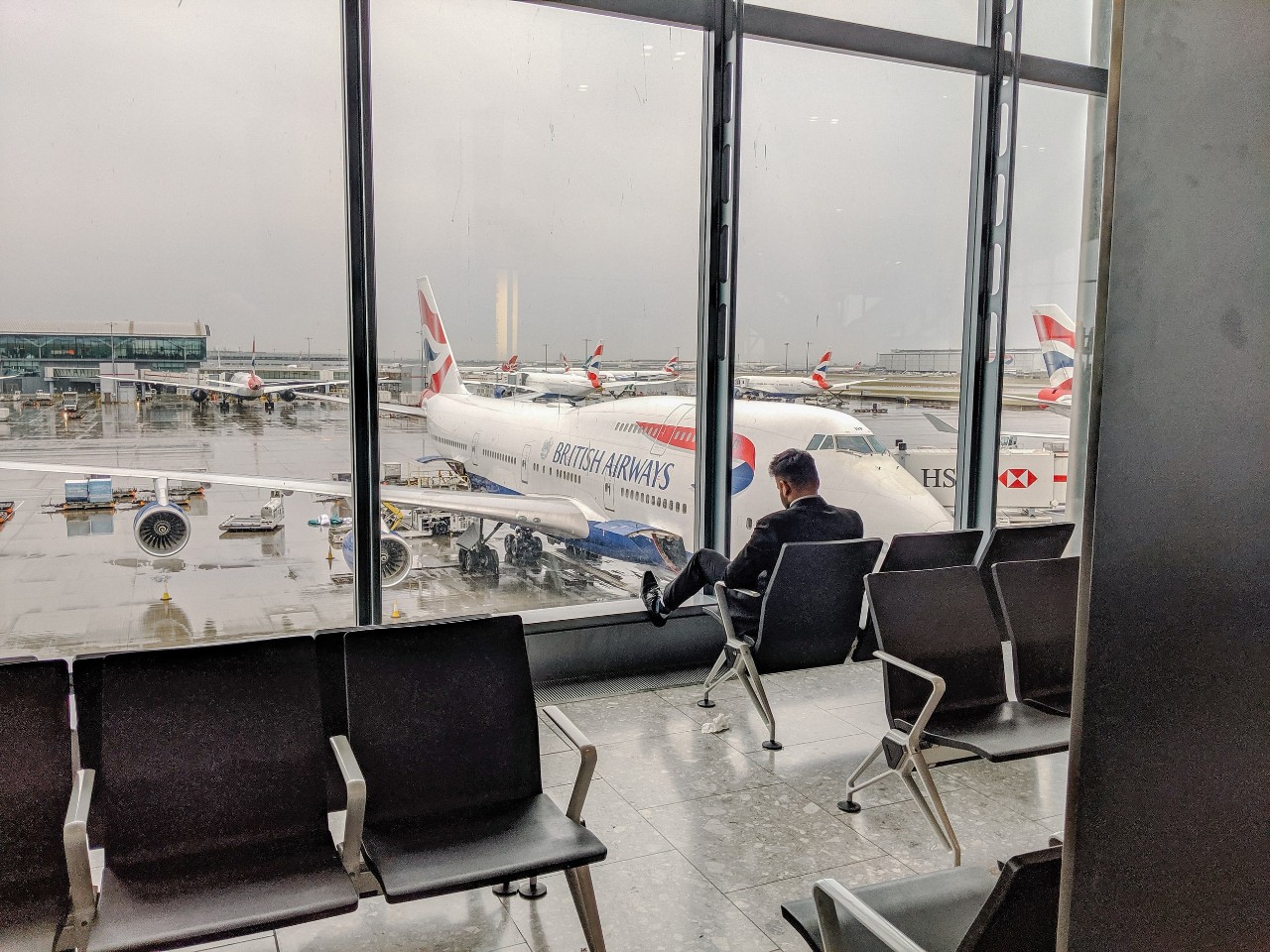 A man waits at an airport terminal overlooking an airliner.