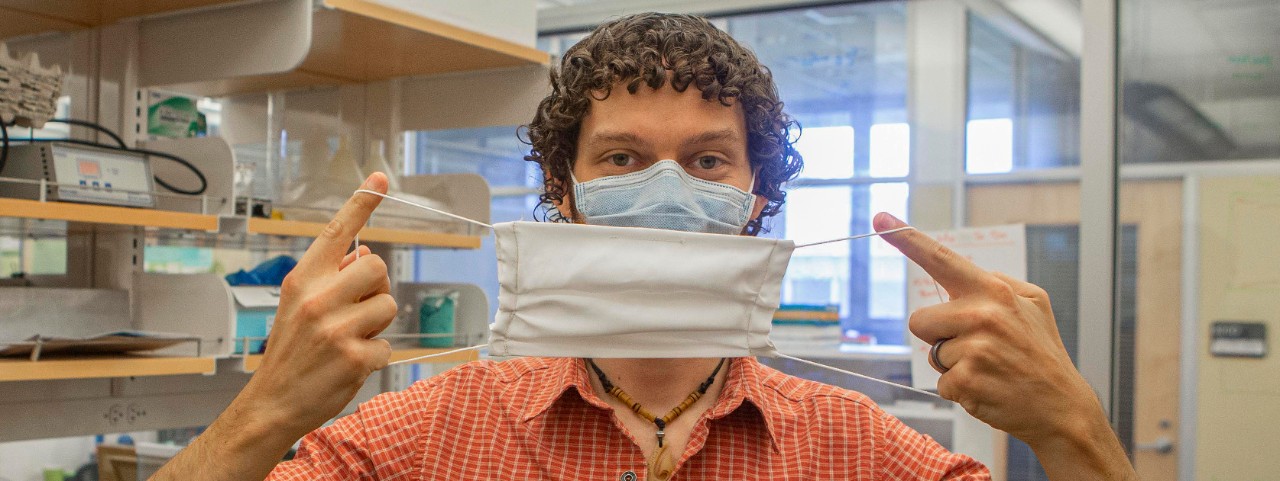UC postdoctoral researcher Adam Parlin holds a silk mask up to his masked face.