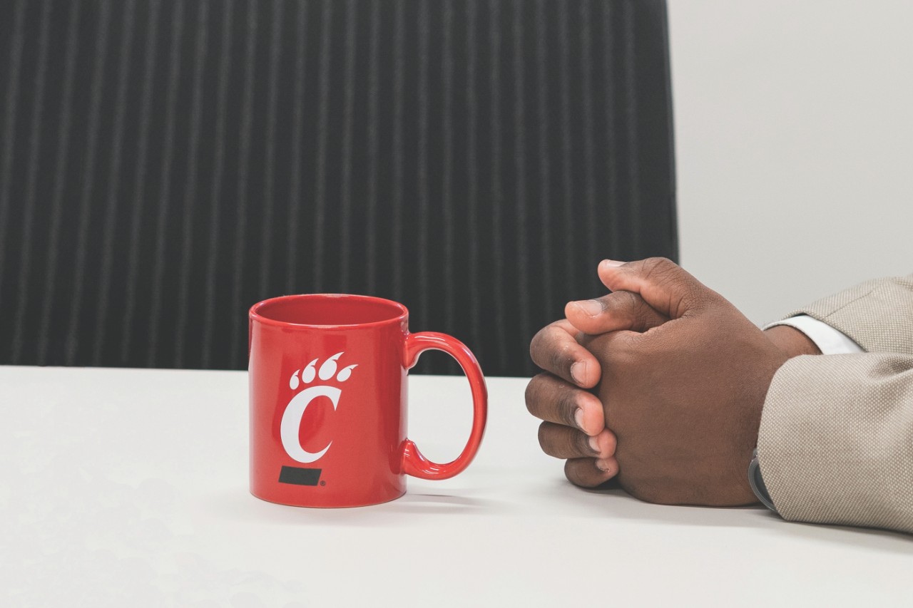 Red C-paw mug on desk with man's crossed hands