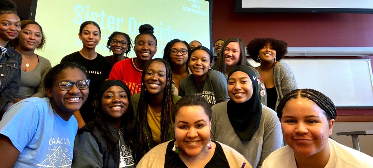 A group of students pose in front of a digital screen