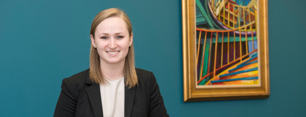 Katelyn Johnson pharmacist in the college standing in front of a blue/green wall with an abstract painting in the background 