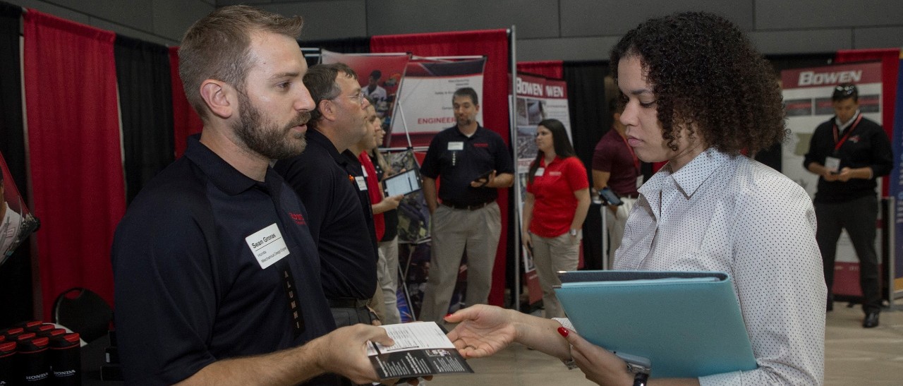 A recruiter hands a card to a job seeker at a UC career fair