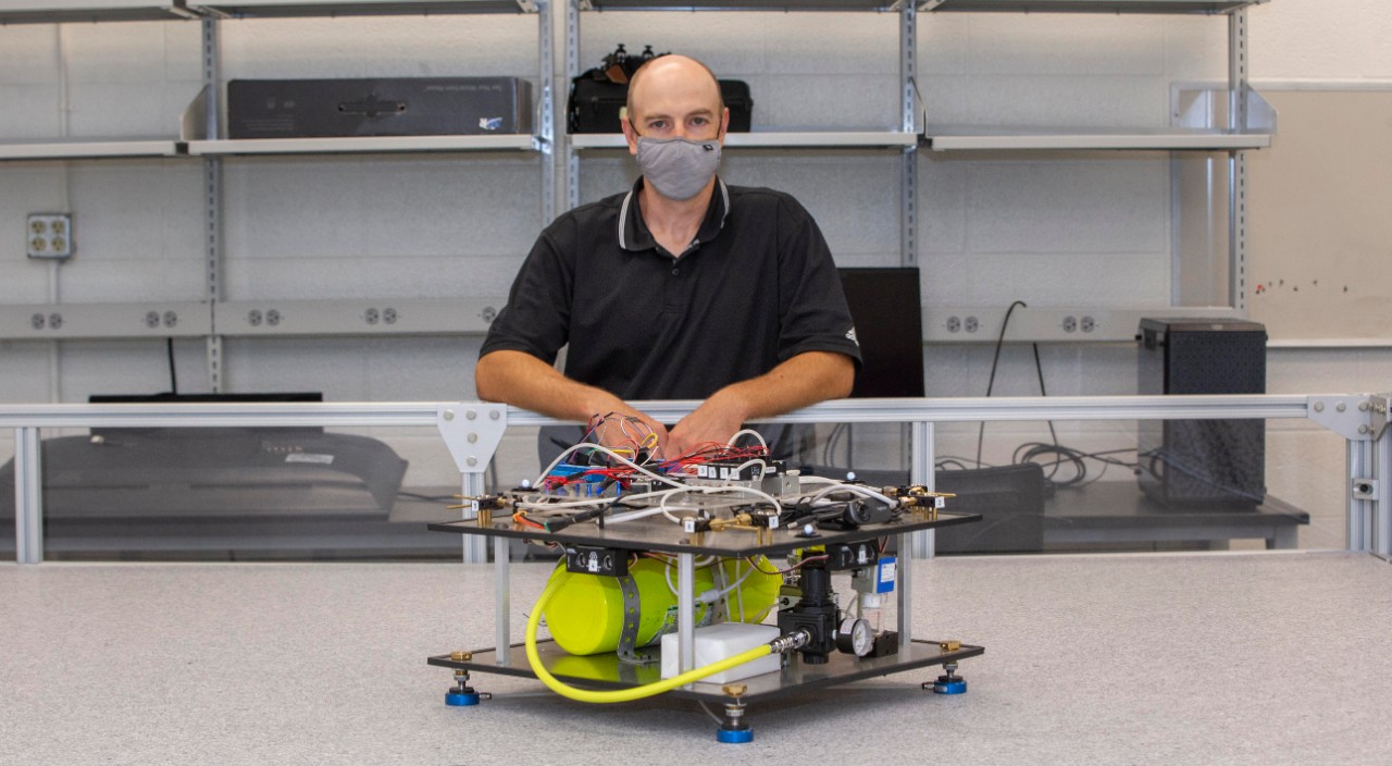 UC student Andrew Barth stands behind a robot in a lab.