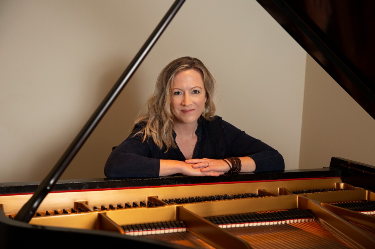 Sarah Hutchings sits at a piano and smiles