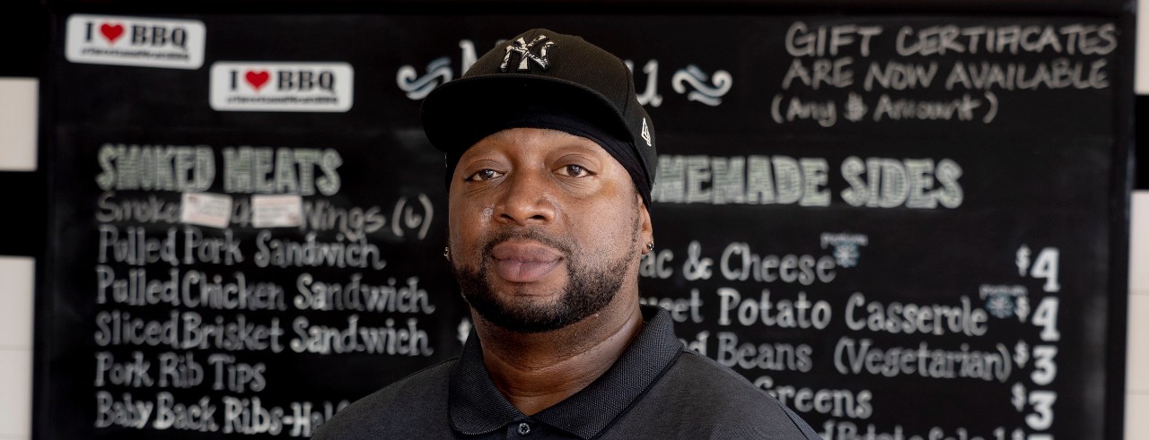 Anton Gaffney, Rising Leader Award recipient, posing for shot with BBQ business menu in background.