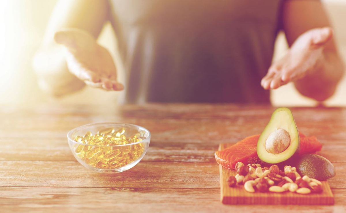 fish oil capsules in a bowl along side a cutting board with foods such as an avocado containing fatty acids 