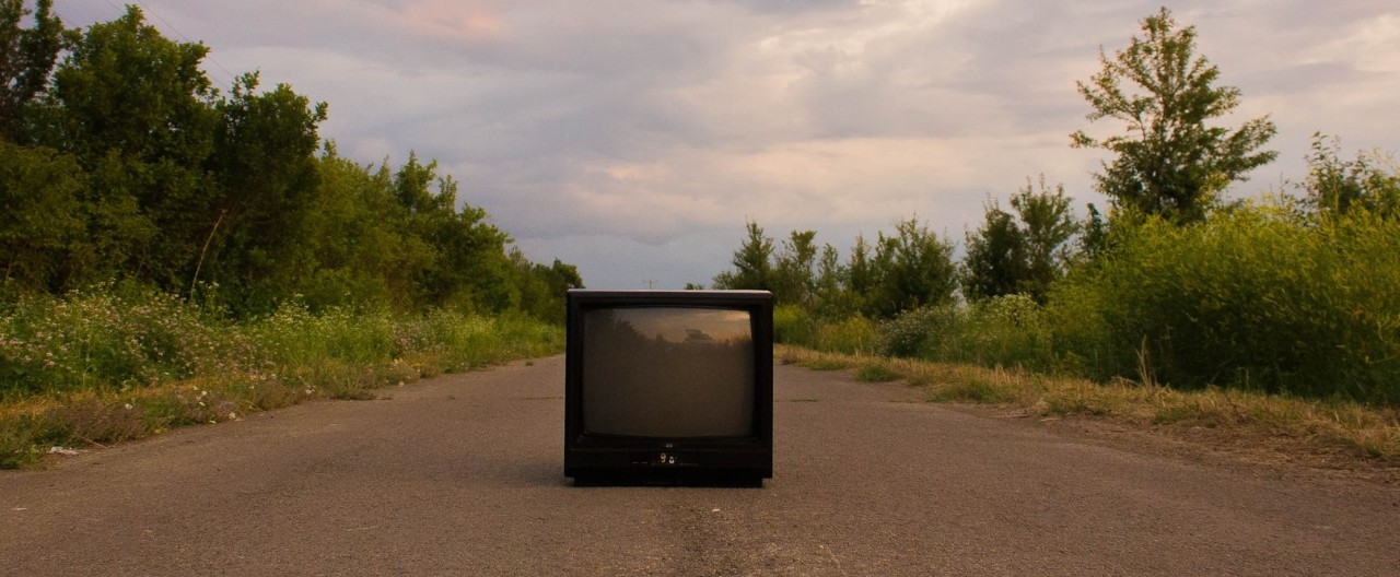 Television sitting in the middle of the road with nature in the bacground