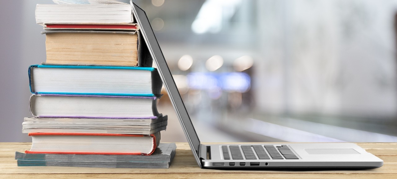 stack of books with laptop leaning against it on wooden table in open nondescript work space