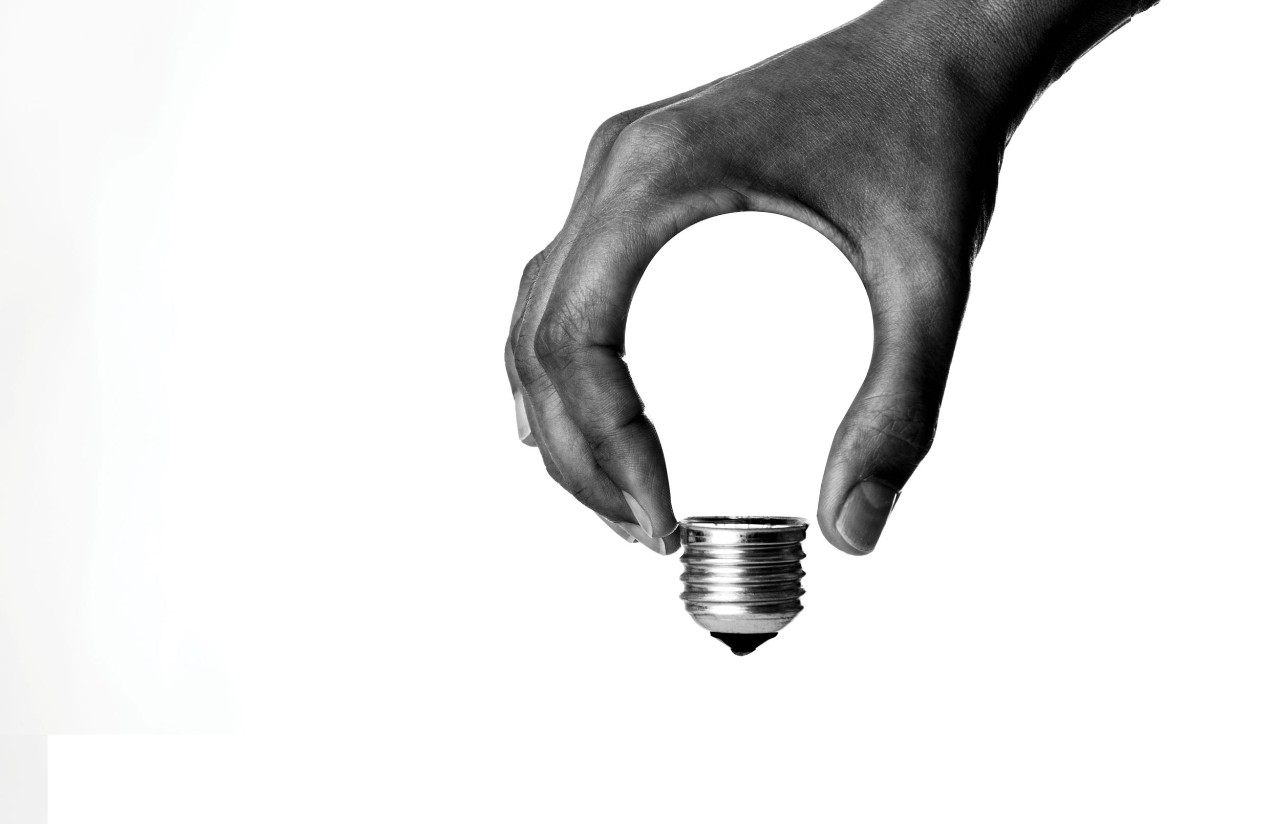 Hand holding a light bulb with fingers and thumb forming the lightbulb shape