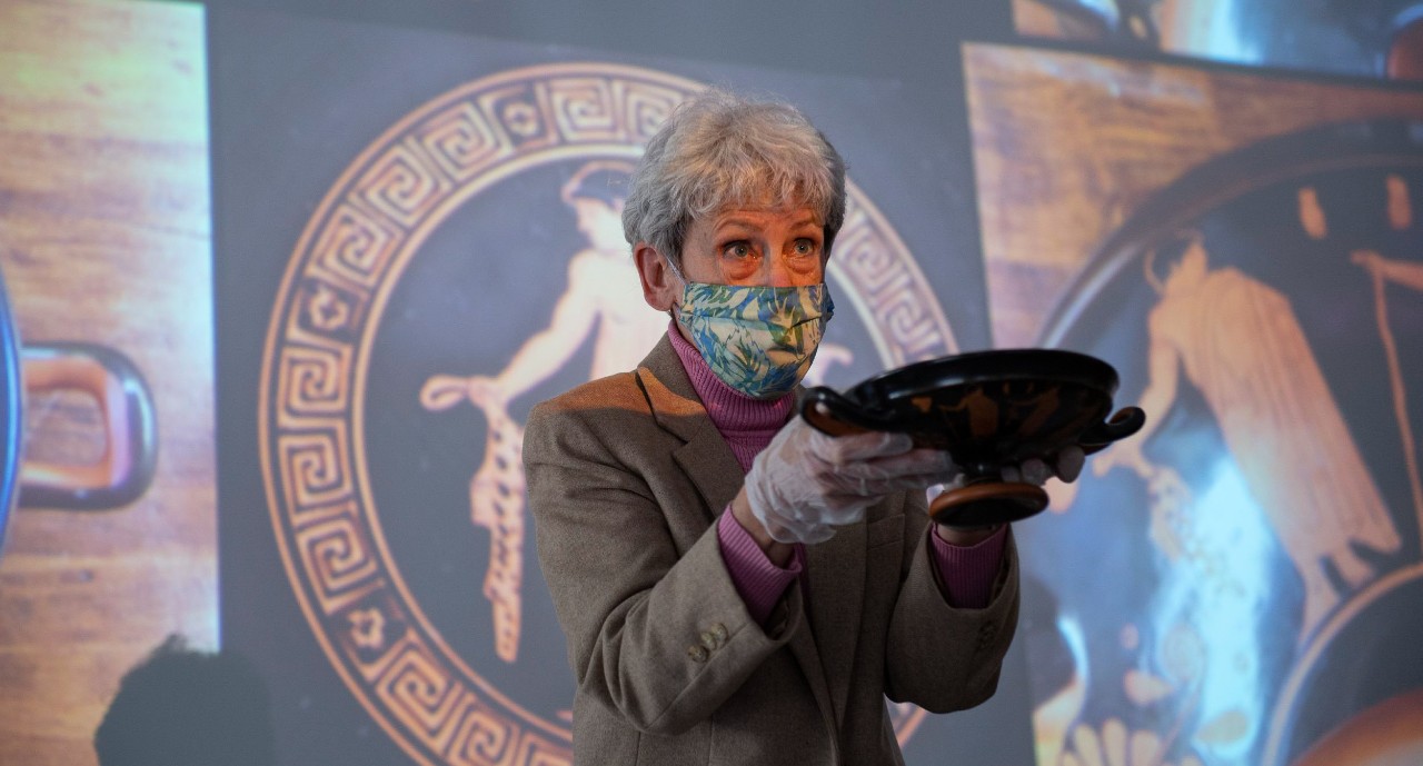 UC professor Barbara Burrell wearing a face mask holds up an ancient Greek cup in her latex-gloved hands.