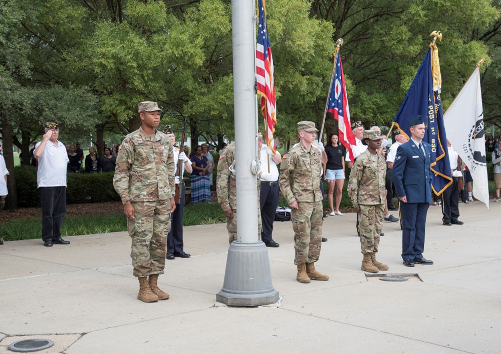 Students and members of military standing at attention during an outdoor flag ceremony