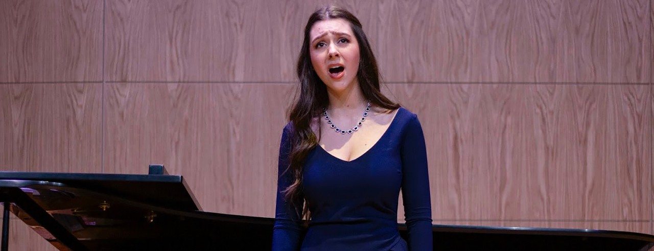 A woman sings on stage with a piano in the background