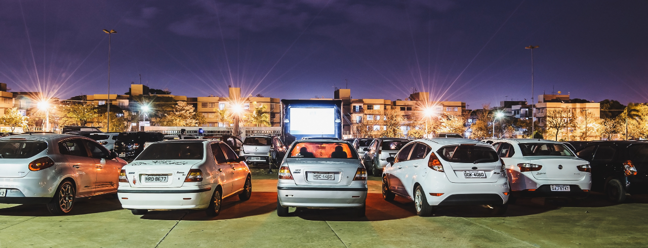 rows of cars in a parking lot, facing a large lit movie screen