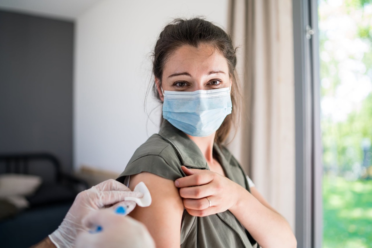 A woman wearing a facemask and looking at the camera gets a vaccine shot