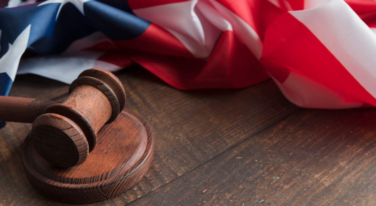 A wood gavel rests on a desk below an American flag