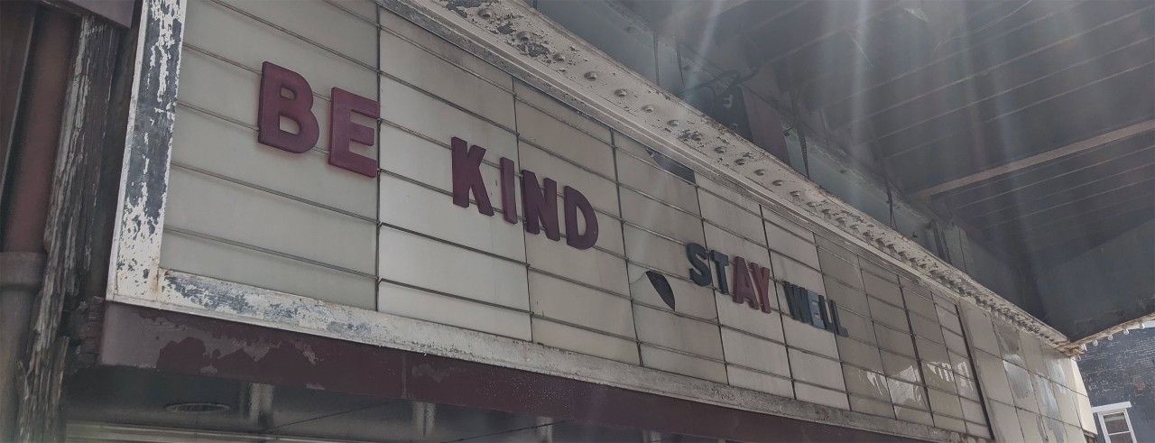 The marquee of a theater reads "Be kind, Stay well."