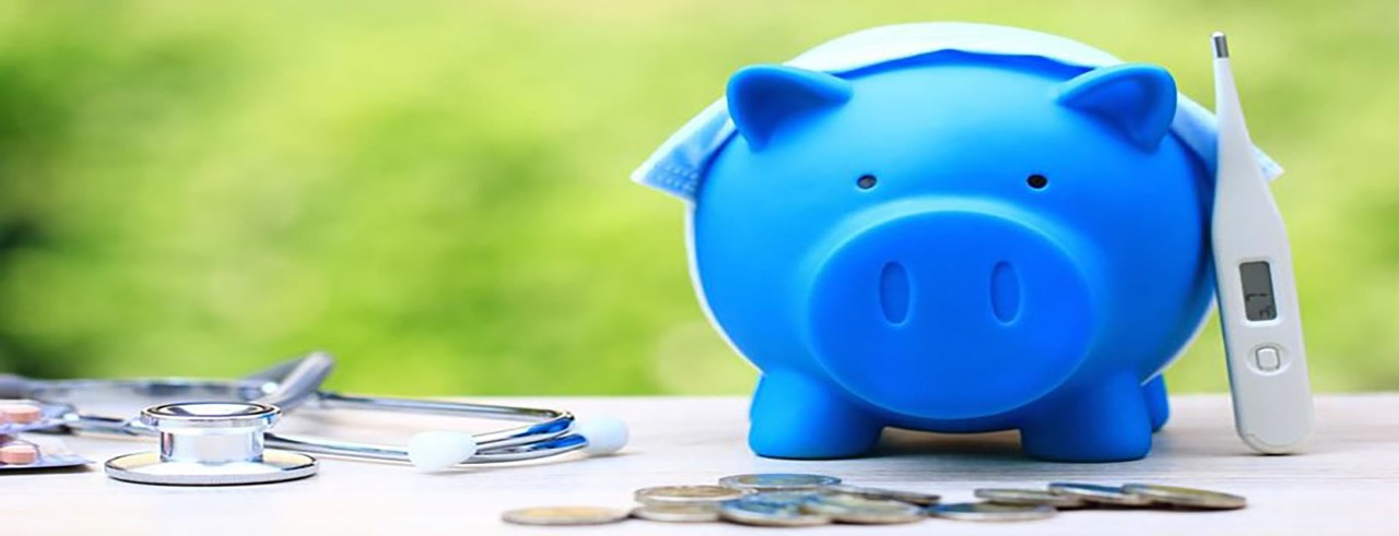 blue piggy bank with some coins and a stethoscope and thermometer