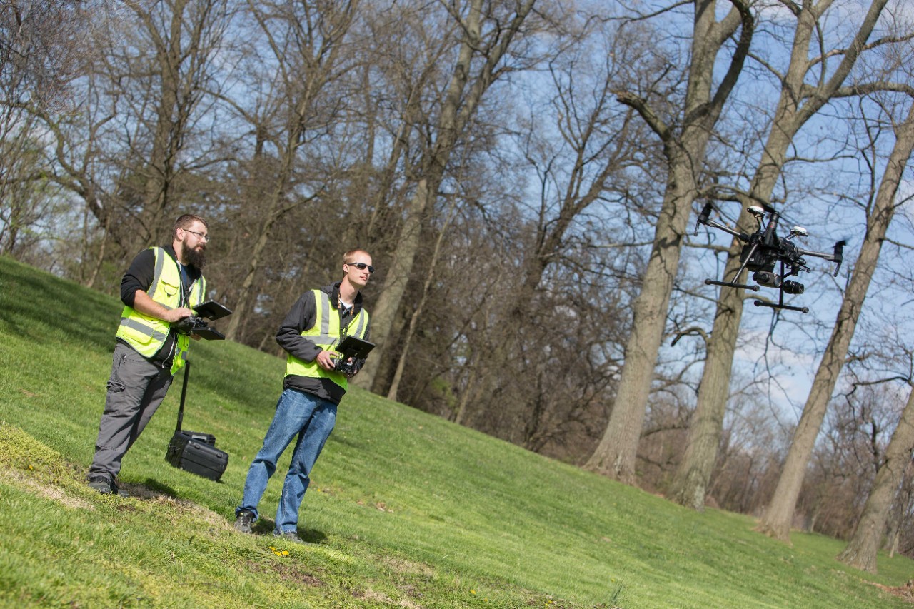 Two people in safety vests fly a drone.