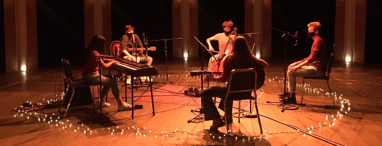 Musicians in masks sit in a circle as the perform