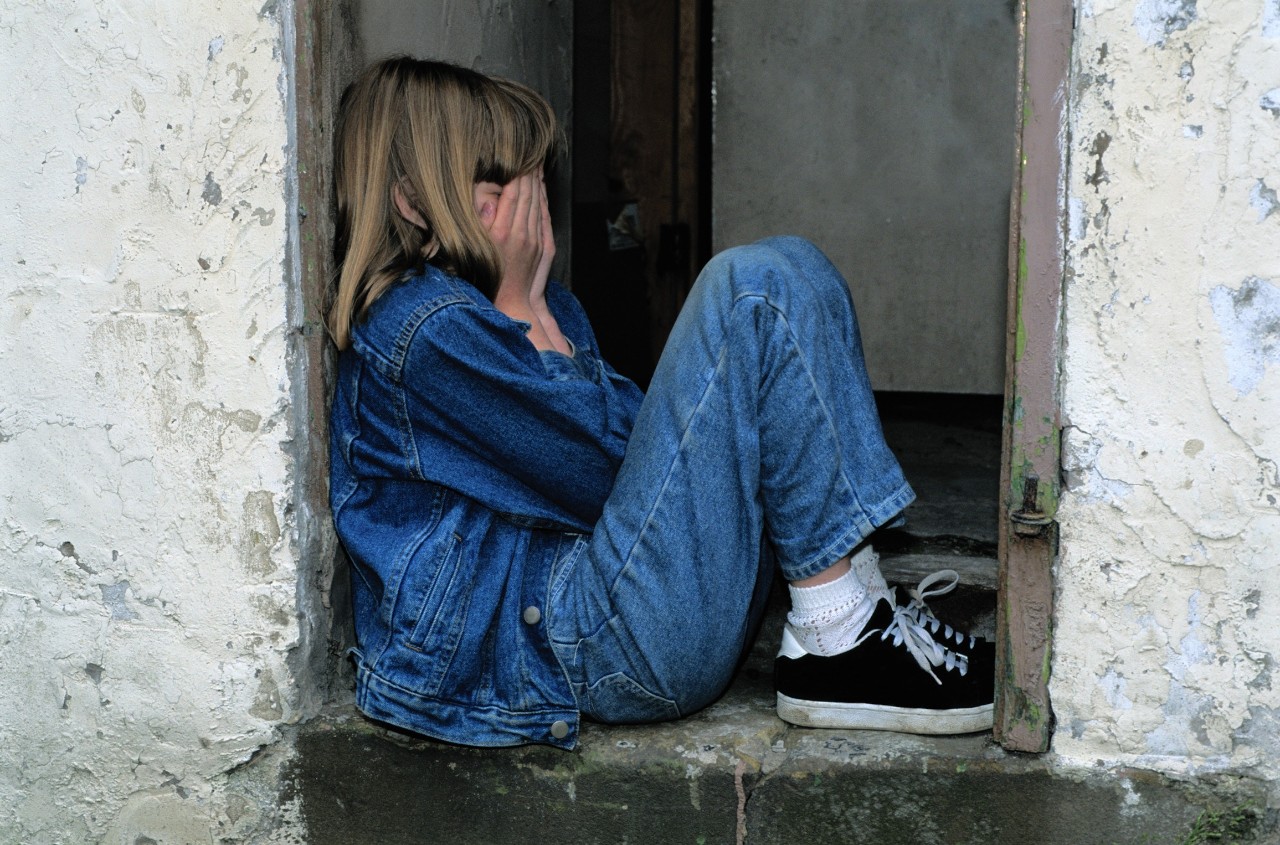 A young girl sits in a doorway with her head in her hands