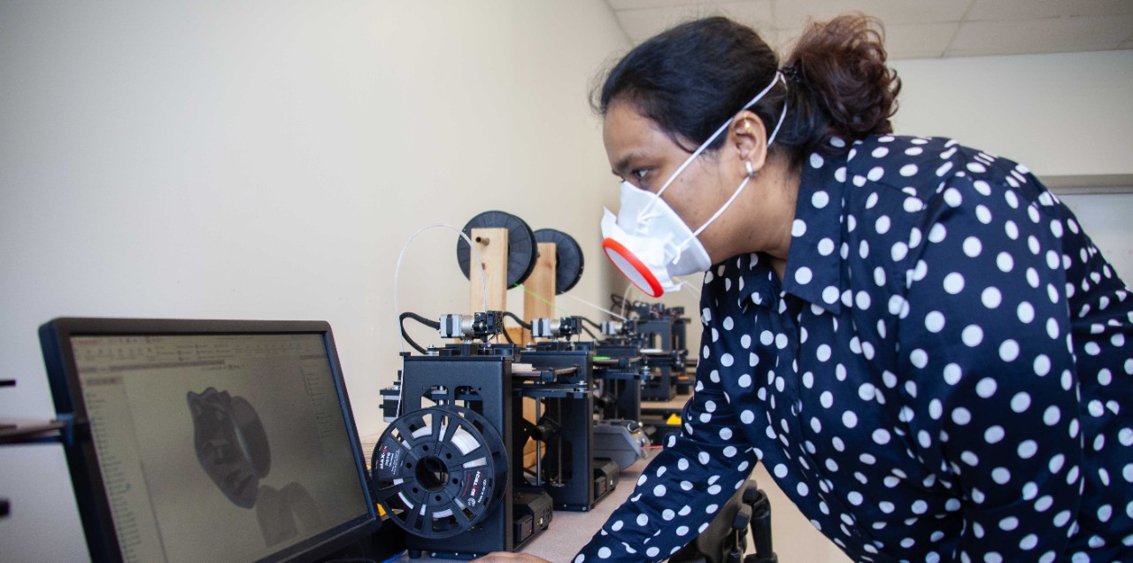 A UC student wearing a custom face mask looks at a laptop image of the design.