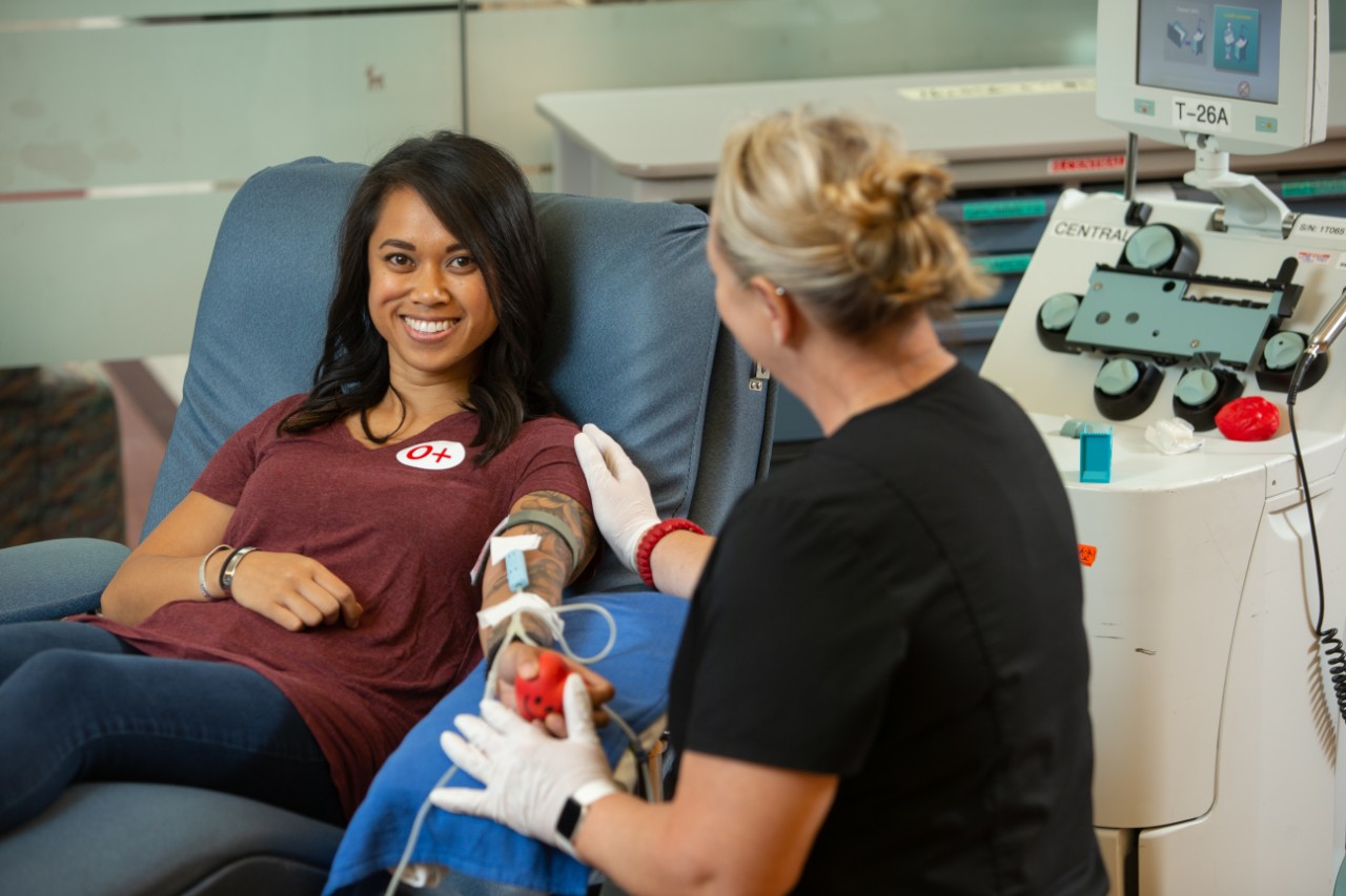 Young woman donating blood and smiling at camera with Hoxworth employee 
