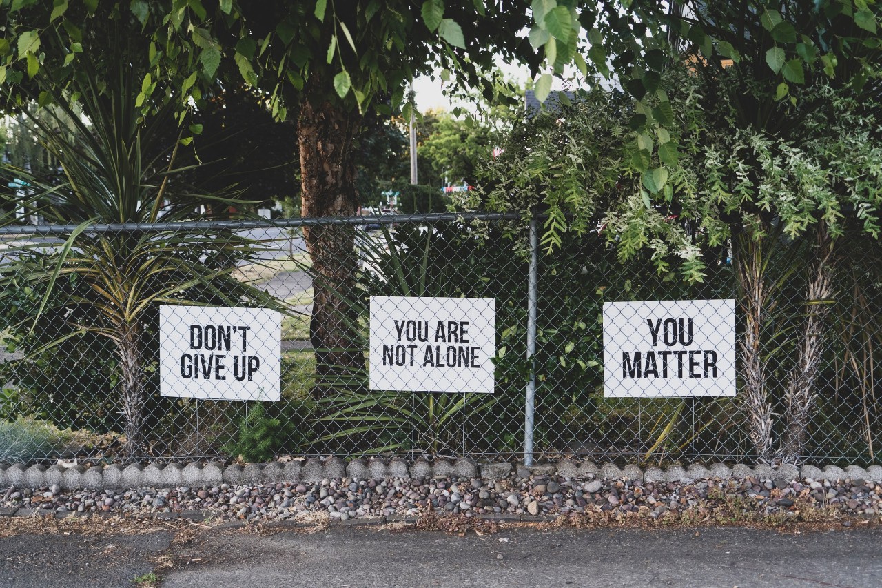 signs on a fence with words of encouragement for mental health: You matter, don't give up