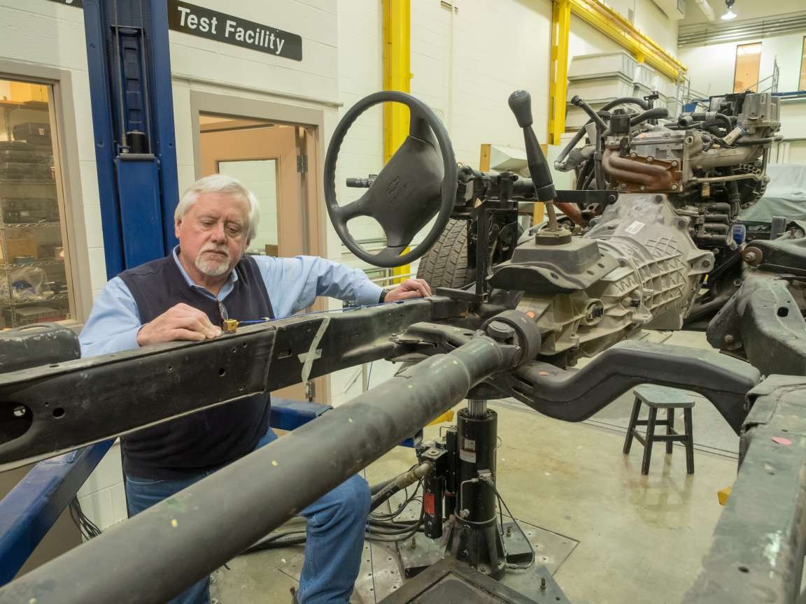 UC professor emeritus Randall Allemang stands next to a car chassis in the Structural Dynamics Research Laboratory.