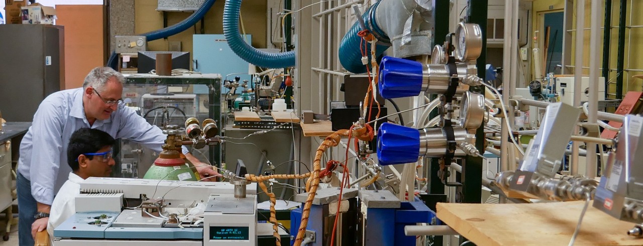 two men sitting in a lab filled with equipment, looking at a computer