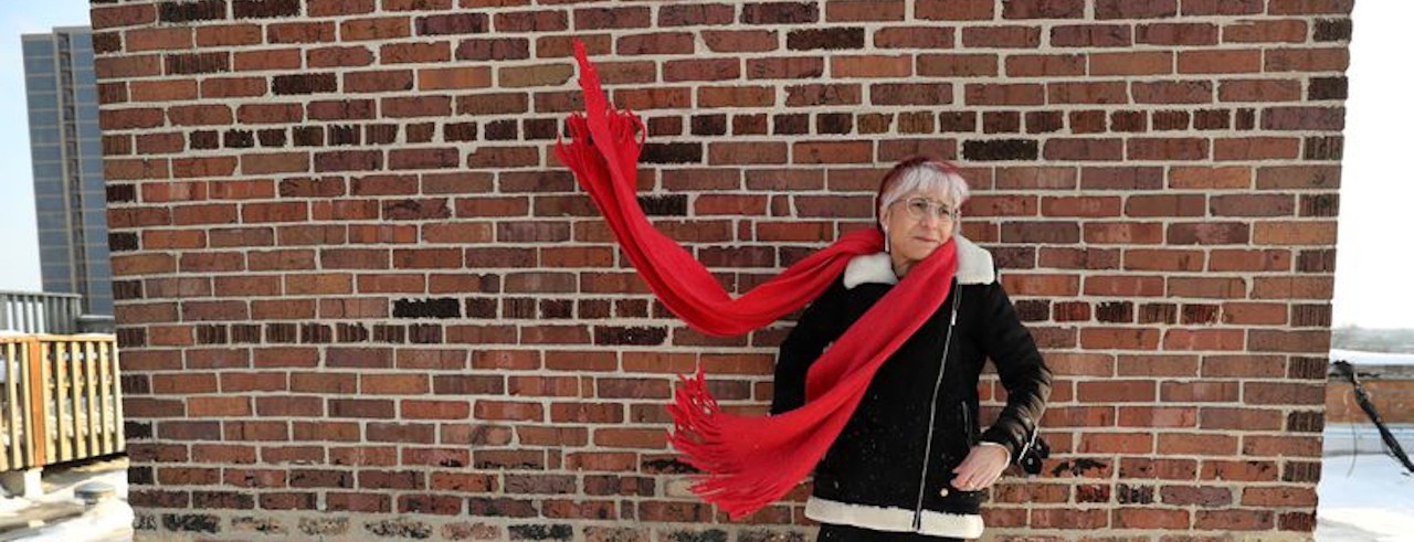 Riva Lehrer poses outside with a red scarf blowing in wind