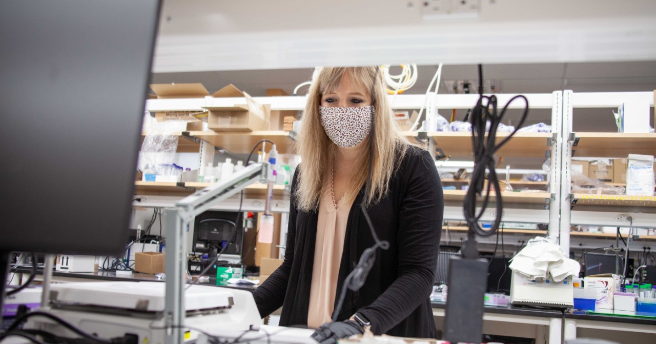 Ashley Ross wearing a face mask and gloves poses for a photo in her lab.