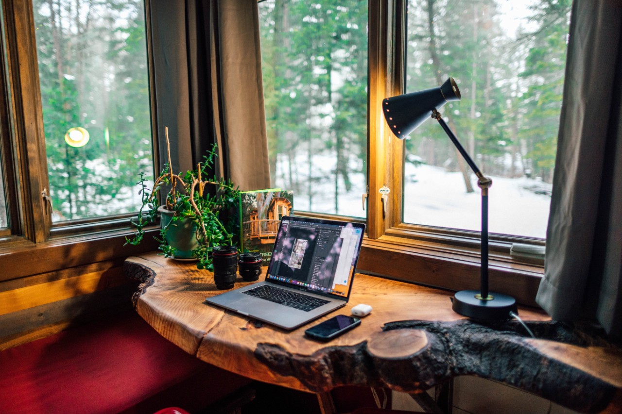 A home office workspace with a laptop on a desk in the corner of a room with windows on both sides