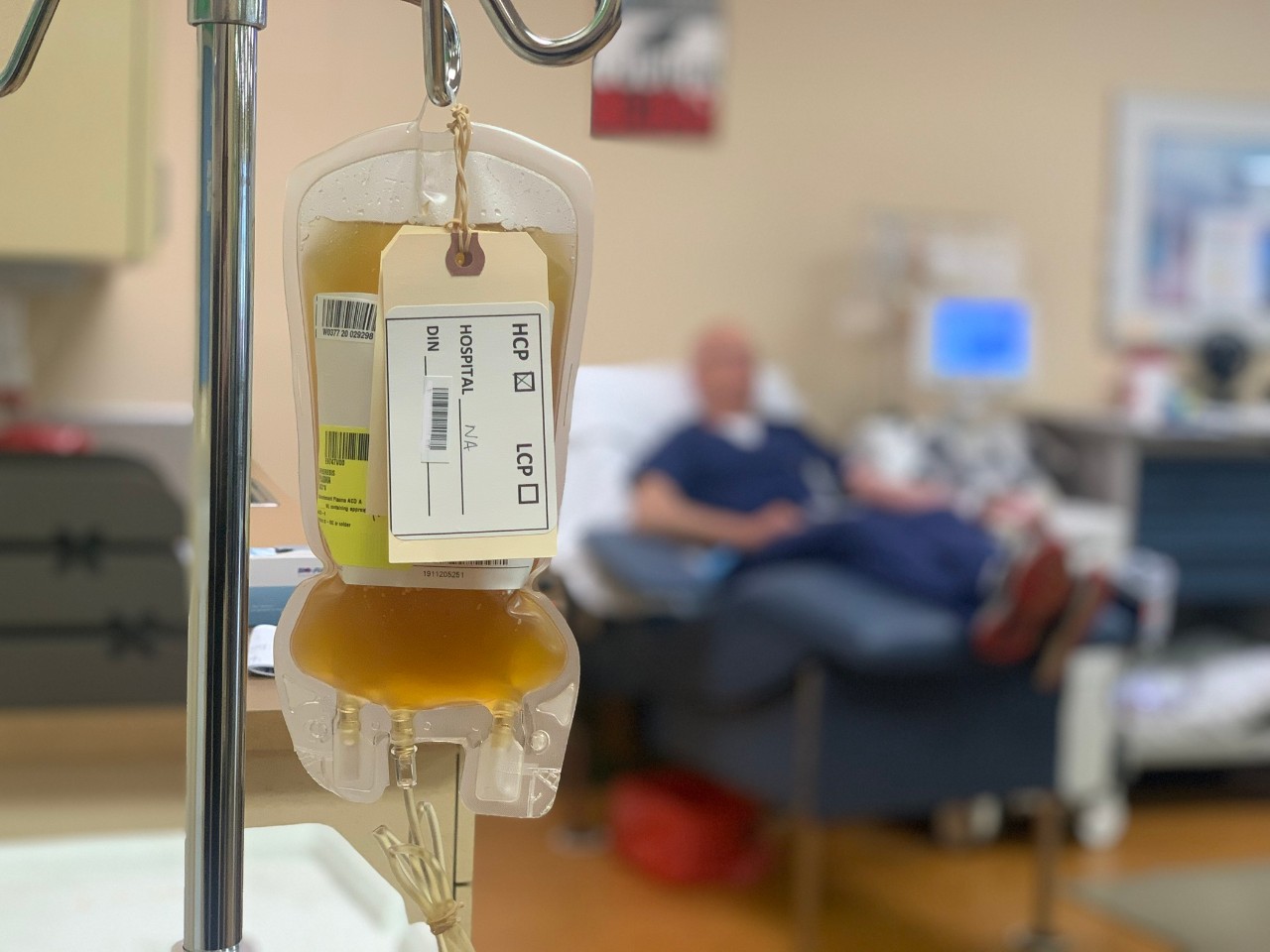 Bag of convalescent plasma hanging on a rack with donor in background
