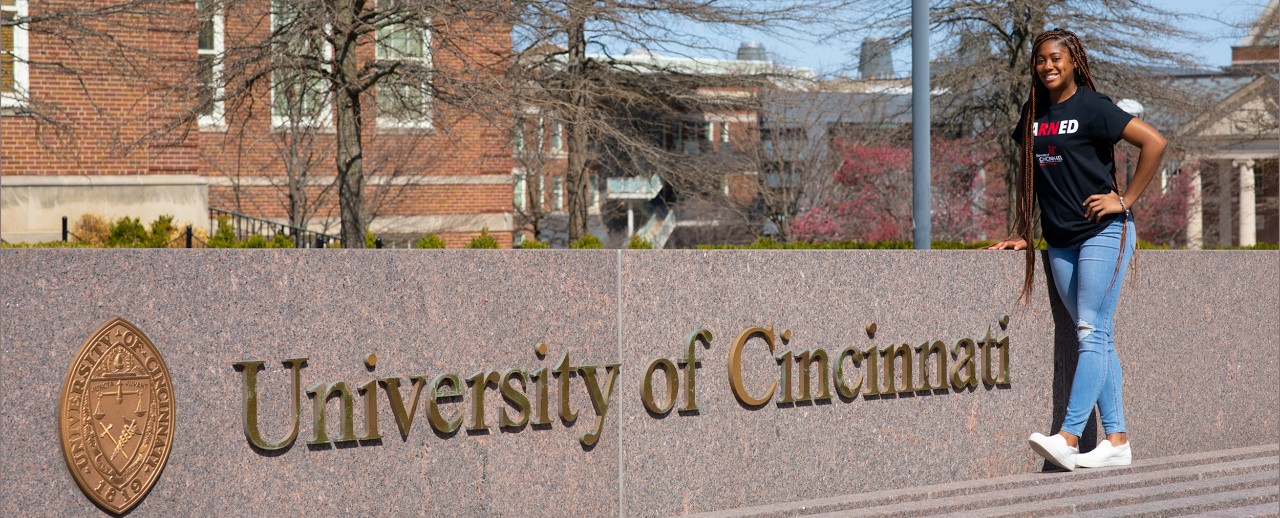 Alex Lewis stands along the UC fountain and sign